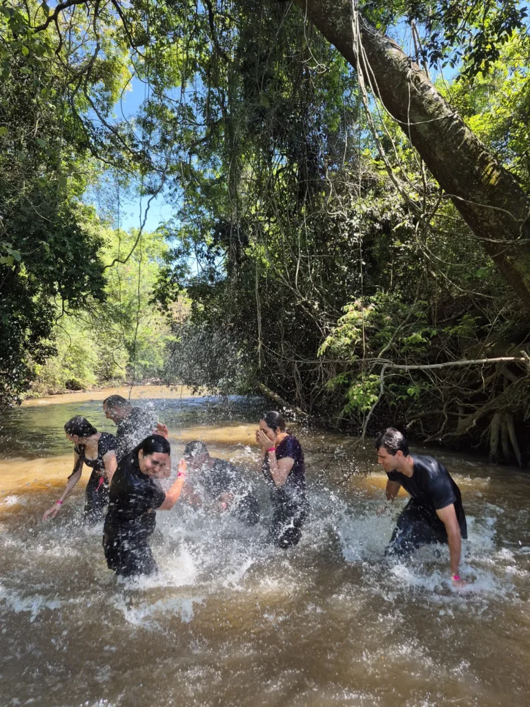 Grupo se divertindo e jogando água dentro do Rio Pinheirinho, em meio à mata.