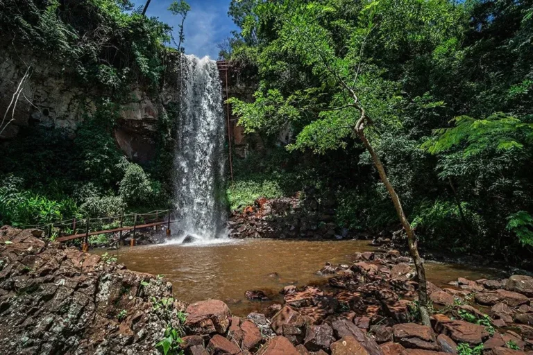 Cachoeira 3 Quedas, com uma queda alta caindo em um poço cercado de mata e pedras.