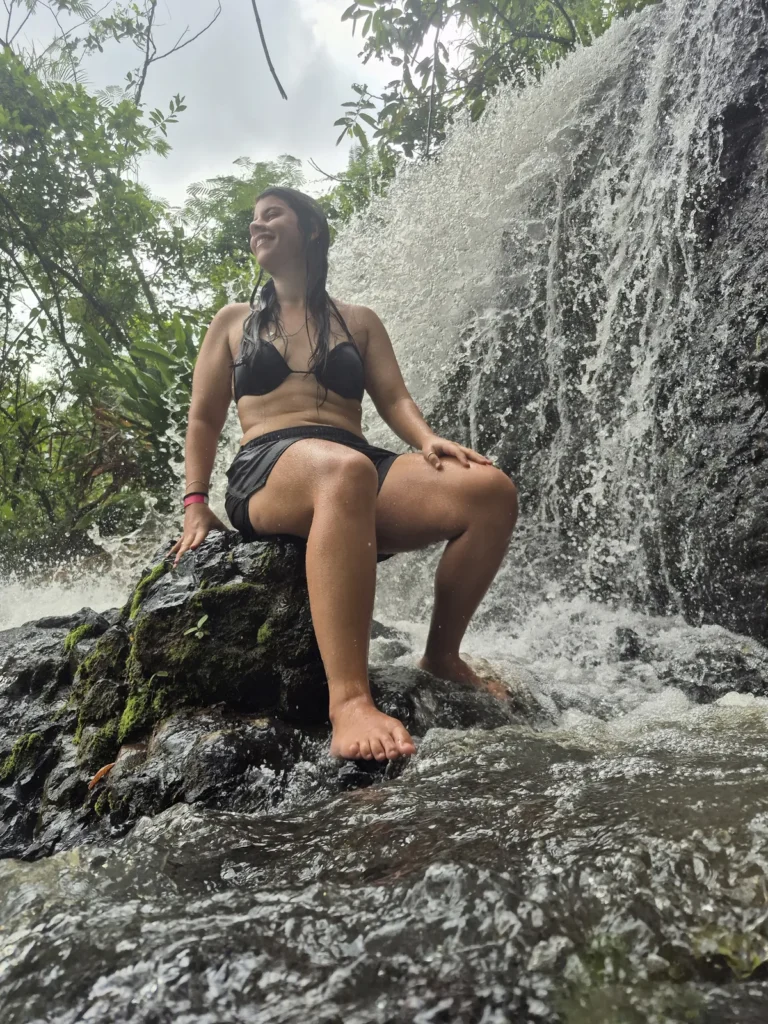 Mulher sentada em uma pedra ao lado da cascata da Cachoeira Santa Maria, com mata ao redor.