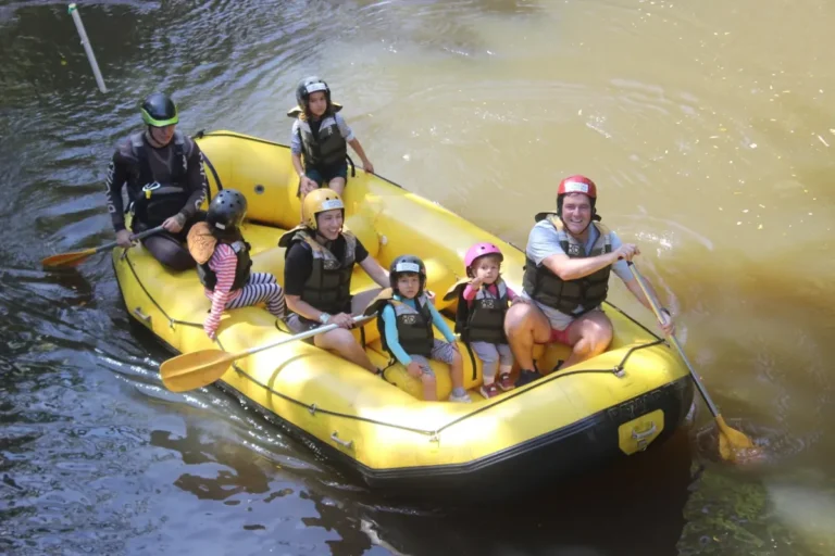 Família de capacete e colete remando em um bote amarelo no trecho tranquilo do mini rafting.