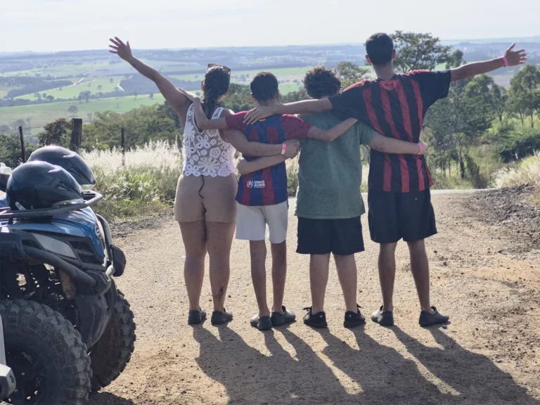 Grupo de quatro pessoas de costas, abraçadas, olhando a vista do mirante da Serra Monte Cristo, ao lado dos quadriciclos.