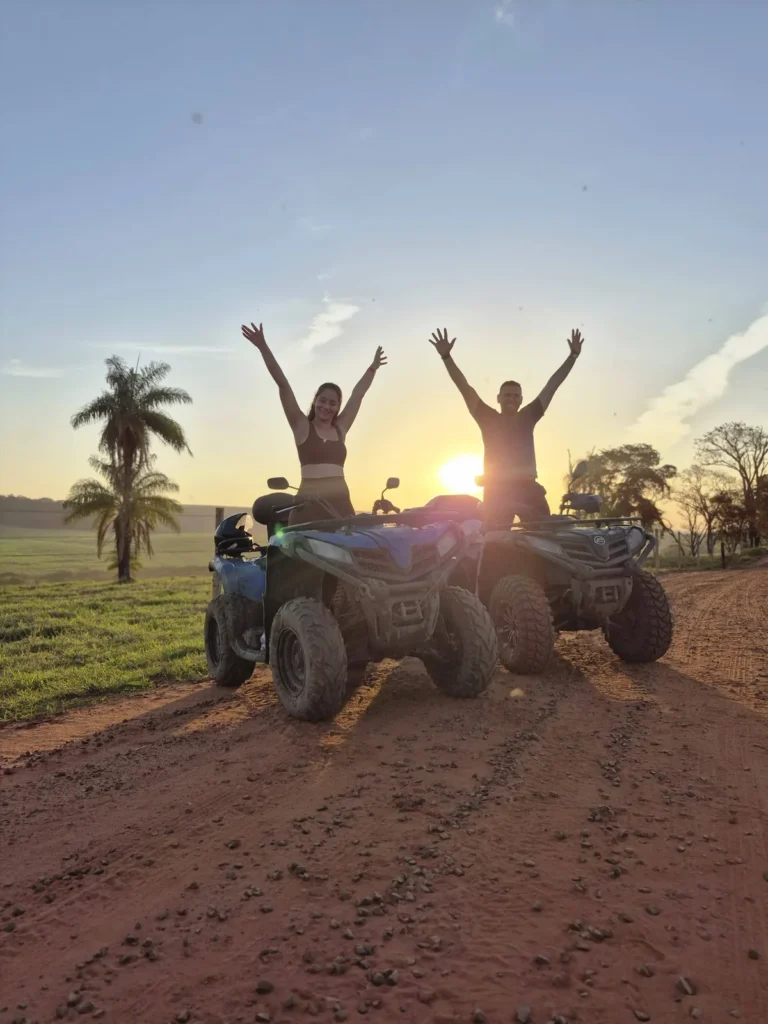 Grupo de braços abertos sobre os quadriciclos em uma estrada de terra durante o pôr do sol.