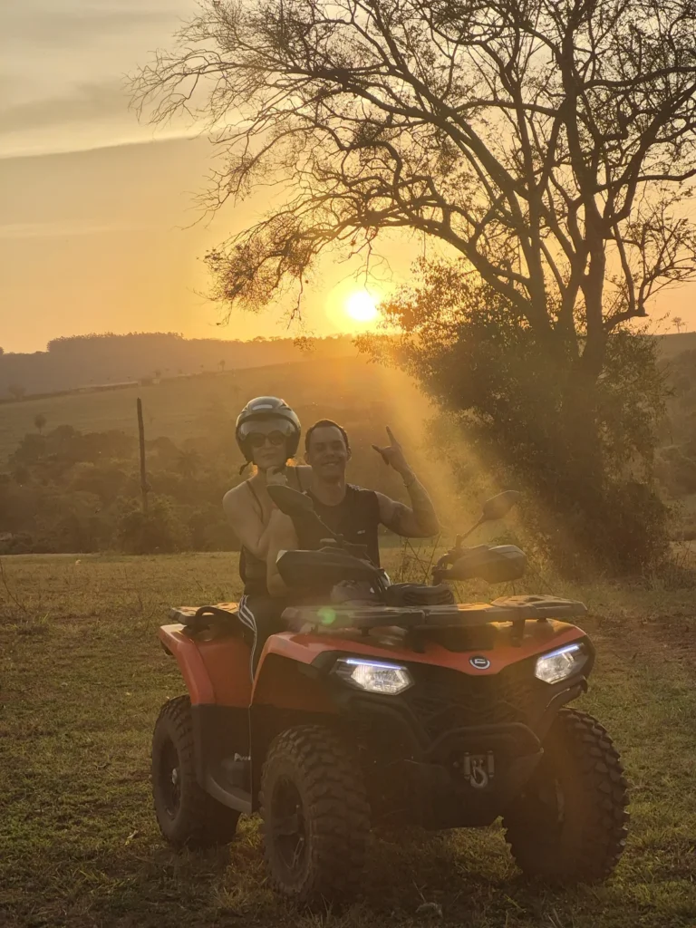 Piloto de capacete no quadriciclo, com raios de sol do fim de tarde passando entre as árvores.