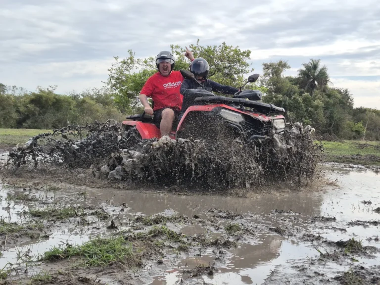 Quadriciclo vermelho atravessando um trecho de lama, levantando barro, no roteiro do Rio Pinheirinho.