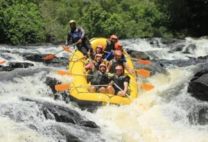 Bote amarelo de rafting com participantes de capacete descendo uma corredeira do Rio Jacaré Pepira.
