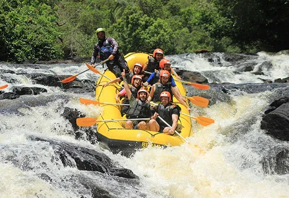 Bote amarelo de rafting com participantes de capacete descendo uma corredeira do Rio Jacaré Pepira.