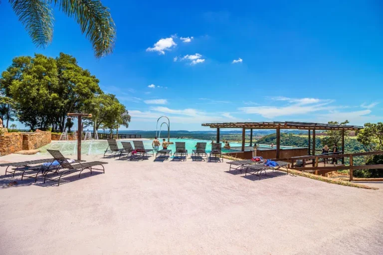 Área de lazer do Recanto das Cachoeiras, com piscina, espreguiçadeiras, quiosque e coqueiros sob céu azul.